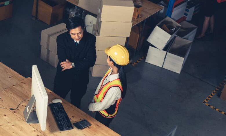 the manager and the warehouse employee are standing near the computer